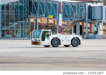 Airplane tow truck near passenger boarding bridge Airplane tow truck near passenger boarding bridge 119351887