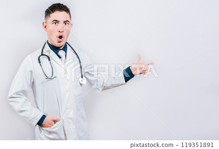 Amazed doctor pointing a promo looking at camera. Surprised young doctor pointing side isolated 119351891