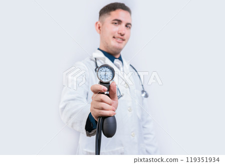 Latin doctor showing blood pressure monitor isolated. Young doctor holding tensiometer on isolated background 119351934
