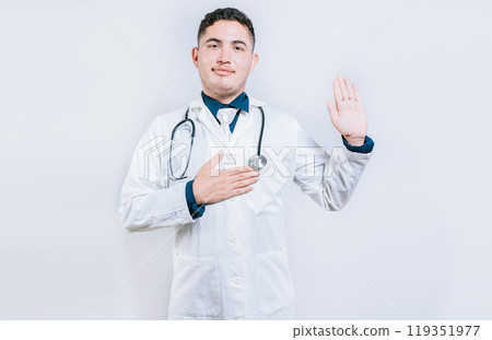 Young doctor raising hand and swearing isolated. handsome doctor making oath and promise isolated Young doctor raising hand and swearing isolated. handsome doctor making oath and promise isolated 119351977