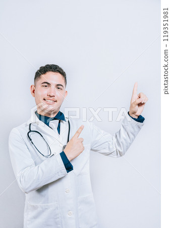 Handsome doctor pointing a promotion with finger isolated. Happy latin doctor pointing at advertising space isolated 119351981