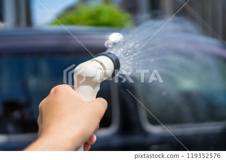 Hands washing a car with a watering nozzle in the parking lot at home 119352576