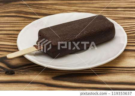 Ice cream in the chocolate glaze lies on a saucer on a wooden table Ice cream in the chocolate glaze lies on a saucer on a wooden table 119353637