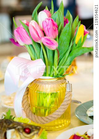Colorful Tulips in a Decorative Jar Centerpiece at a Dining Table With Gourmet Dishes 119354621