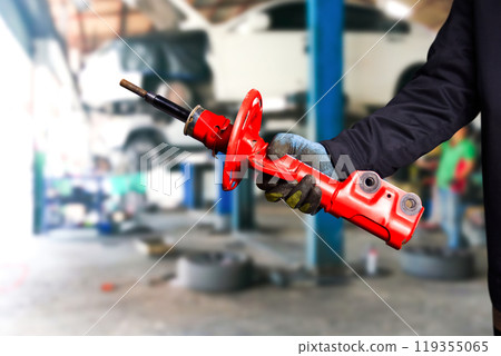 Auto mechanic holding a old red shock absorber in repair garage Auto mechanic holding a old red shock absorber in repair garage 119355065