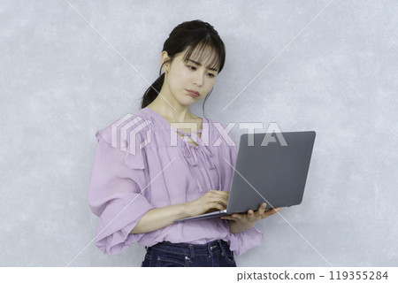 一位年輕女子手裡拿著筆記型電腦站著,看起來很困擾 一位年輕女子手裡拿著筆記型電腦站著,看起來很困擾 119355284