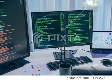 Software development office Workstation setup with multiple monitors displaying code and development diagrams during a nighttime coding session Software development office Workstation setup with multiple monitors displaying code and development diagrams during a nighttime coding session 119357192
