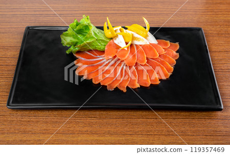 slicing appetizer of red fish slices on a black plate on a wooden table top view slicing appetizer of red fish slices on a black plate on a wooden table top view 119357469