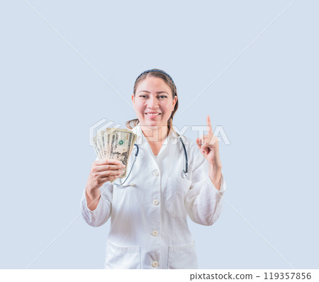 Smiling female doctor holding money and pointing up isolated. Happy young female doctor showing money and pointing at promo up Smiling female doctor holding money and pointing up isolated. Happy young female doctor showing money and pointing at promo up 119357856