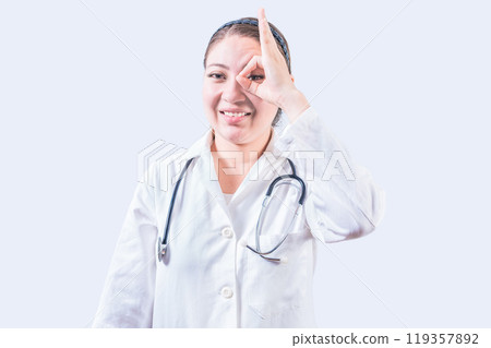 Cheerful female doctor gesturing approval isolated. Young female doctor approving with finger on isolated background 119357892