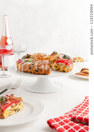 A wreath shaped cake with candied fruit and nuts on a cake stand, with wine glasses in the background 119358064