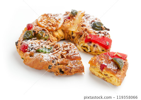 A partially sliced wreath shaped cake decorated with candied fruit, nuts, and powdered sugar A partially sliced wreath shaped cake decorated with candied fruit, nuts, and powdered sugar 119358066