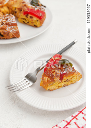 A slice of colorful cake with candied fruit and a fork on a white plate, paired with a checkered napkin 119358067