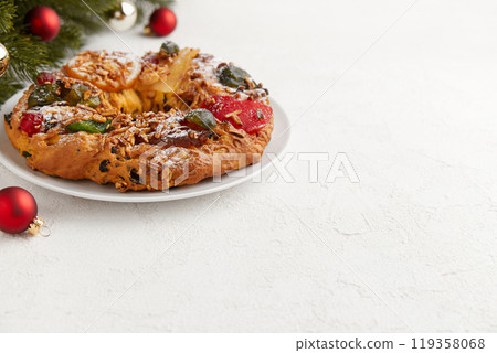 A wreath shaped cake with candied fruit and nuts, displayed with Christmas ornaments and a tree A wreath shaped cake with candied fruit and nuts, displayed with Christmas ornaments and a tree 119358068