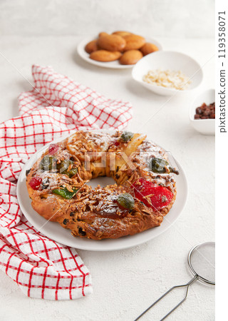 A wreath shaped cake with candied fruit and nuts on a white plate, surrounded by bowls and napkins A wreath shaped cake with candied fruit and nuts on a white plate, surrounded by bowls and napkins 119358071