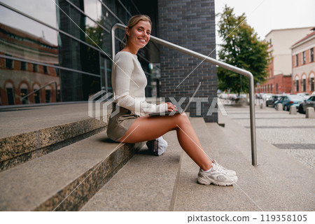 A young woman happily working on her laptop while enjoying the beautiful outdoors 119358105