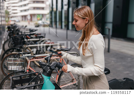In a vibrant, bustling urban environment filled with life, a woman is unlocking her bicycle In a vibrant, bustling urban environment filled with life, a woman is unlocking her bicycle 119358117
