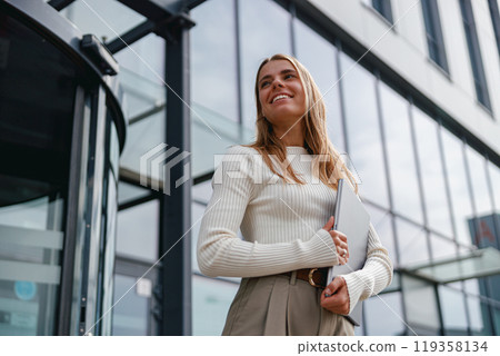 A Confident Businesswoman Smiling Brightly Outside a Modern Office Building in the City 119358134