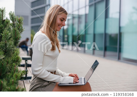 A Young Woman Engaged in Working Outdoors on Her Laptop in a Stylish Modern Setting A Young Woman Engaged in Working Outdoors on Her Laptop in a Stylish Modern Setting 119358168