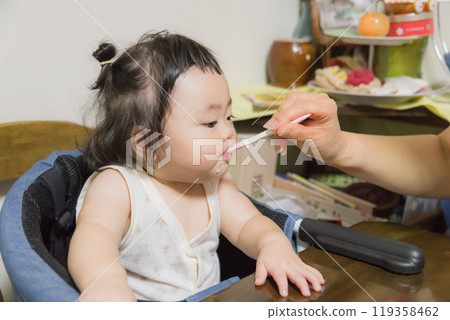 [Baby with tied hair eating baby food] 119358462
