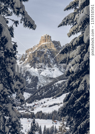 Sassongher Mountain rises above Colfosco framed by snow-covered trees, bathed in soft evening light Sassongher Mountain rises above Colfosco framed by snow-covered trees, bathed in soft evening light 119358561