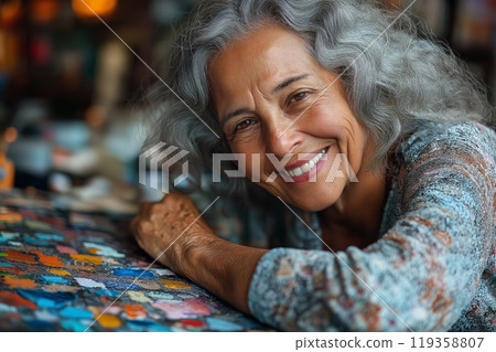 A joyful elderly woman with grey hair leans on a colorful table during an art activity in a nursing home 119358807