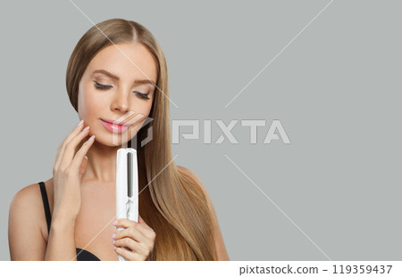 Pretty woman with hair straightener iron in studio isolated on white background. Haircare, wellness 119359437