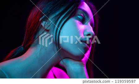 Portrait of beautiful young Korean girl posing against black background with blue and pink neon lights 119359597