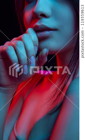 Close-up of lips and hand. Cropped image of beautiful young woman posing in red neon lights against black background Close-up of lips and hand. Cropped image of beautiful young woman posing in red neon lights against black background 119359613