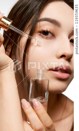 Beautiful young Korean girl applying facial serum, taking care after flawless skin. Skincare routine focused on hydration and nourishment. Beautiful young Korean girl applying facial serum, taking care after flawless skin. Skincare routine focused on hydration and nourishment. 119359635