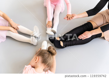 Ballet dancers wearing pointe shoes sitting in floor stretching during classical choreography training Ballet dancers wearing pointe shoes sitting in floor stretching during classical choreography training 119359742
