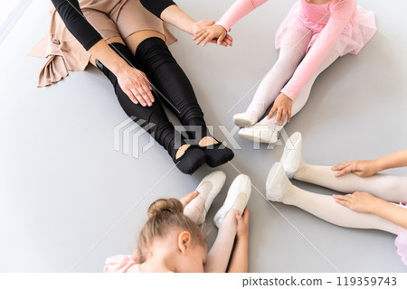 Unrecognizable woman and little girls sitting in circle and doing stretching at ballet school Unrecognizable woman and little girls sitting in circle and doing stretching at ballet school 119359743