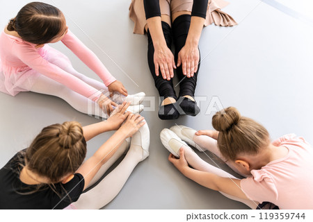 Little girls with teacher stretching legs together in ballet class 119359744