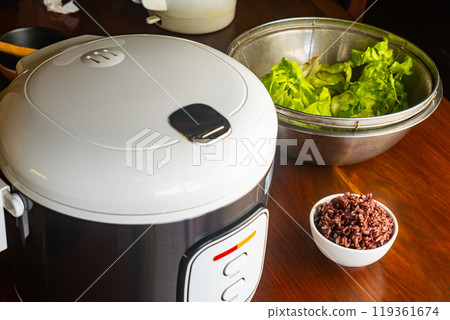 High angle view of electric rice cooker, steamed brown riceberry and fresh green vegetables High angle view of electric rice cooker, steamed brown riceberry and fresh green vegetables 119361674