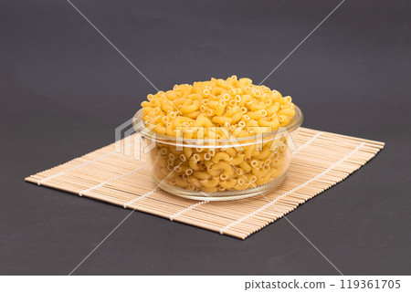 Uncooked Chifferi Rigati Pasta in Glass Jar on Bamboo Mat on Black Background Uncooked Chifferi Rigati Pasta in Glass Jar on Bamboo Mat on Black Background 119361705
