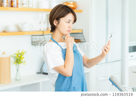 Woman with smartphone in kitchen 119363519