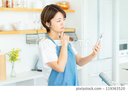 Woman with smartphone in kitchen 119363520