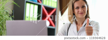 Satisfied doctor shows thumb up gesture sitting at table Satisfied doctor shows thumb up gesture sitting at table 119364628