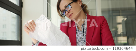 Disappointed female manager reads sheet sitting at table 119364644