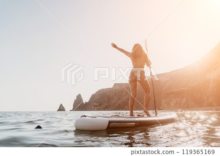 Woman Paddleboarding Ocean Coastline - A woman on a paddleboard in the ocean near a rocky coastline. Woman Paddleboarding Ocean Coastline - A woman on a paddleboard in the ocean near a rocky coastline. 119365169