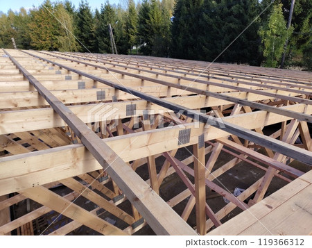 Wide-angle view of roof framing with wooden beams and connector plates, capturing the scale and structure under a clear sky 119366312