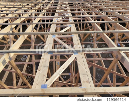 Top view of extensive wooden roof trusses with metal connectors, illustrating the structural complexity and layout of a construction site 119366314