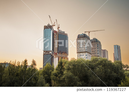 Cityscape. Multi-storey buildings in the rays of the setting sun. Sunset in the city. Construction of skyscrapers. Tower cranes. Moscow 119367227