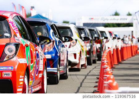 A line of racing vehicles waiting for the ceremonial start of a car race rally 119367516
