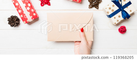 Top view of female hand holding an envelope on wooden background. New Year decorations. Christmas time concept 119368205