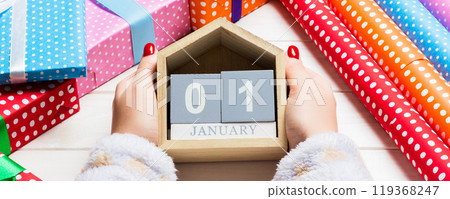 Top view of female hands holding a calendar on wooden background. The first of January. Holiday decorations. New Year concept Top view of female hands holding a calendar on wooden background. The first of January. Holiday decorations. New Year concept 119368247