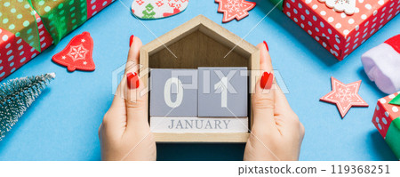 Top view of female hands holding calendar on blue background. The first of January. Holiday decorations. New Year concept Top view of female hands holding calendar on blue background. The first of January. Holiday decorations. New Year concept 119368251