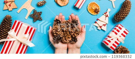 Top view of a heap of pine cones in female hands on blue backround made of festive decorations. Christmas time concept 119368332