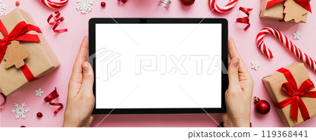 Christmas online shopping from home, female hands holding tablet pc with blank white display top view. woman hand holding tablet with blank screen, Christmas tree and gifts on background 119368441