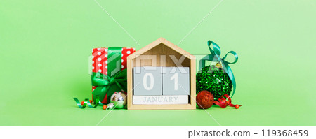 1 january. Christmas composition on colored background with a wooden calendar, with a gift box, toys, bauble copy space 119368459